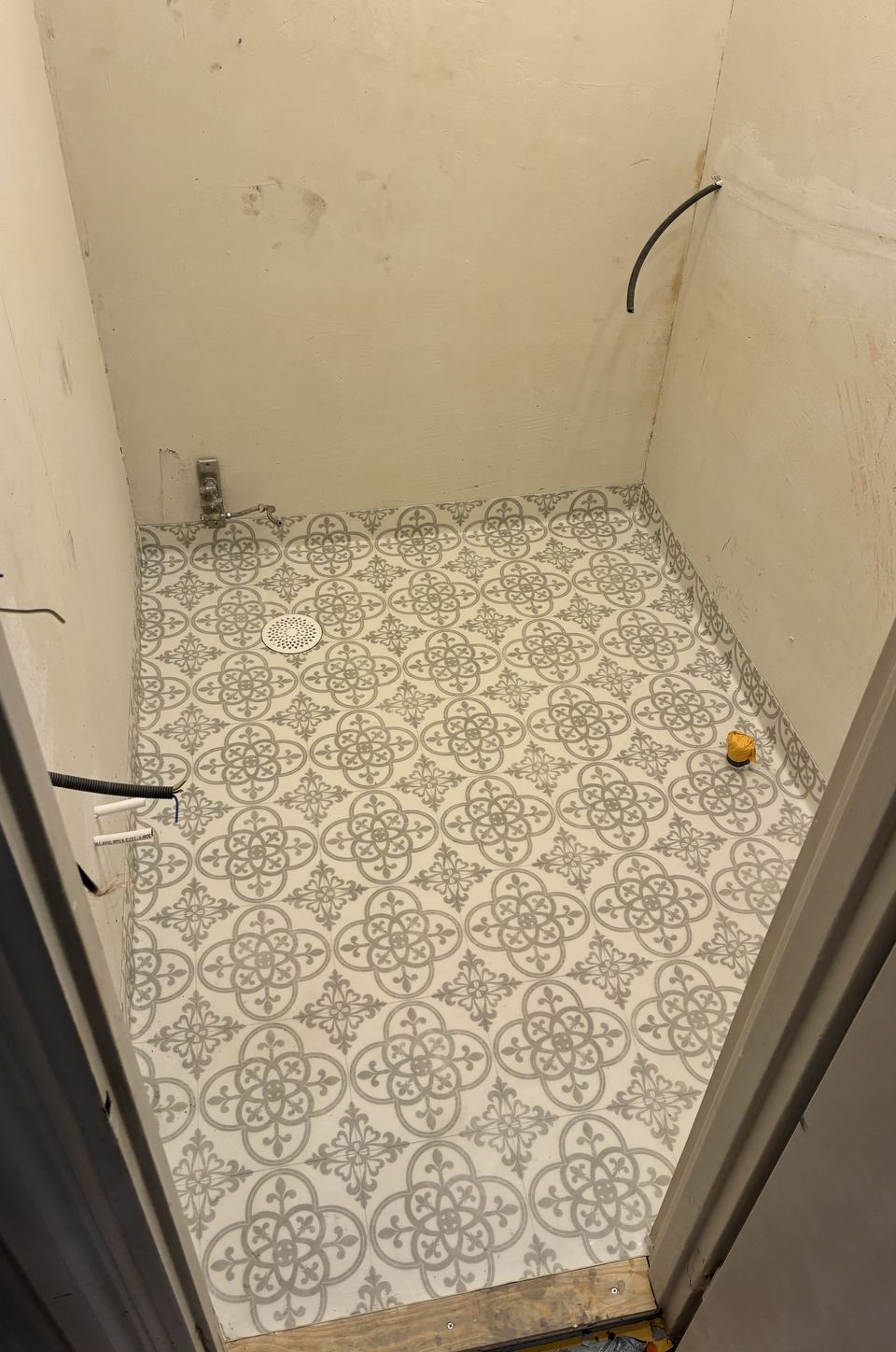 Mönstrad plastmatta med uppvik och golvbrunn i litet våtrum under renovering