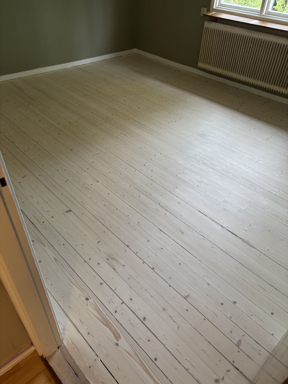 Vitbehandlat plankgolv i rum med gröna väggar